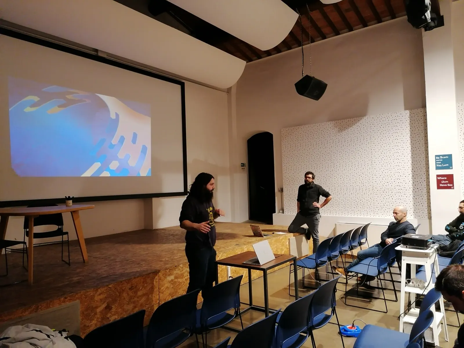 Uno speaker sul palco davanti allo schermo durante la prima edizione